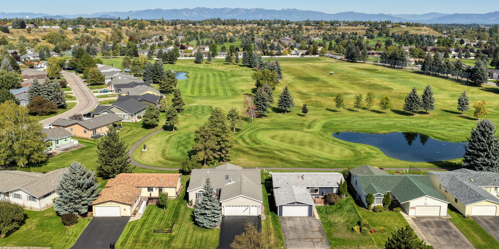 Aerial view of 124 W Nicklaus Ave backing onto the Village Greens course, with the green and pond behind the home and the mountains in the distance