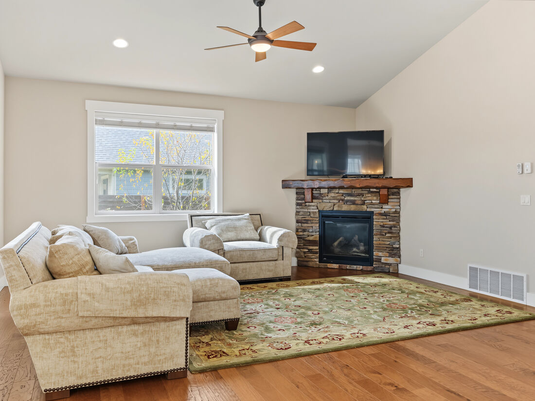 Great room with vaulted ceiling, stone-surround gas fireplace, and engineered hardwood floors
