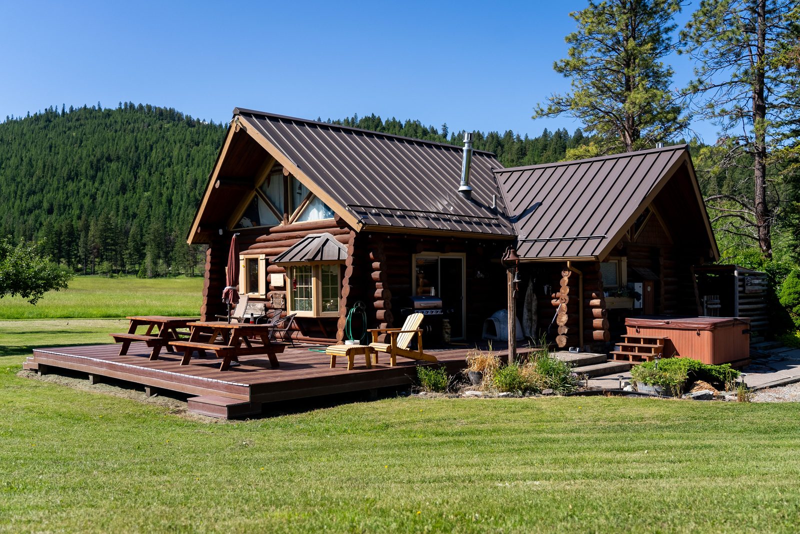 Log home exterior with covered deck and metal roof, framed by evergreens