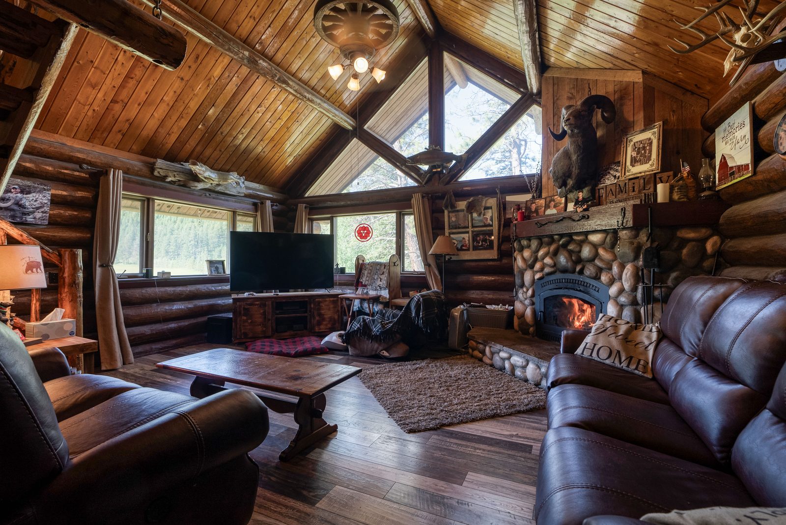 Vaulted log living room with stone fireplace, exposed beams, and large windows
